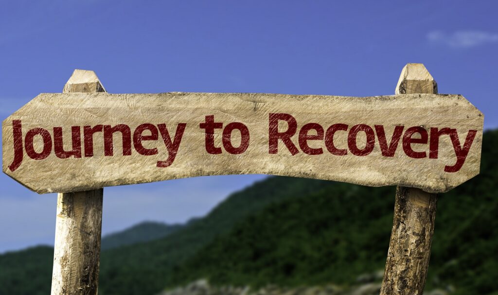A wooden sign with the words journey to recovery against as 